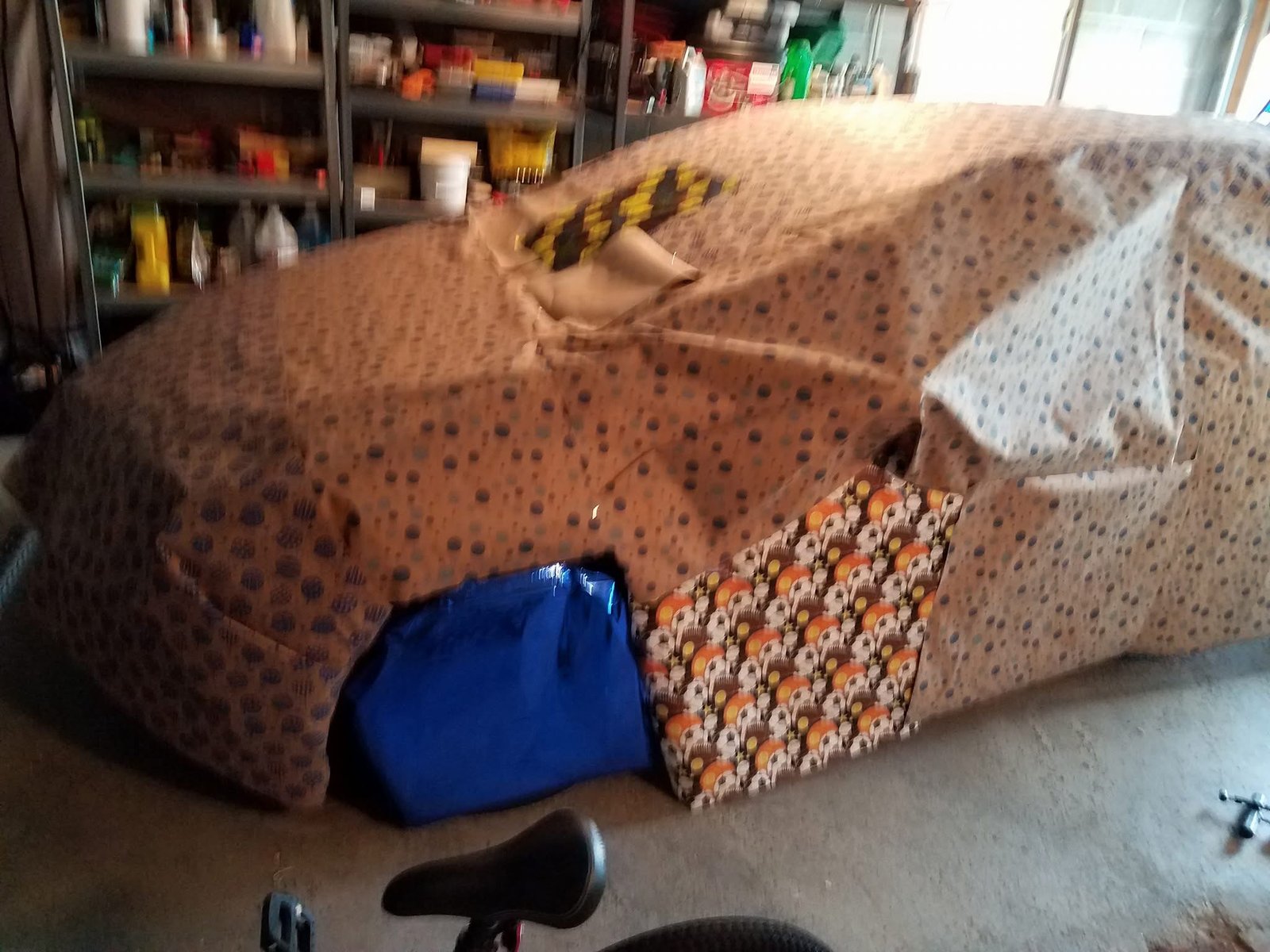 A car in a garage fully wrapped in mismatched wrapping paper.